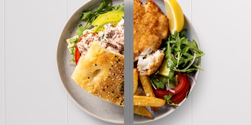 A split-plate meal featuring a creamy tunacado sandwich with avocado on one side, and crispy fish and chips with pesto salad, lemon, and greens on the other.