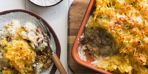 Smoked fish pie served in a baking dish with a portion plated, showing a creamy filling and golden cheesy mashed potato topping.
