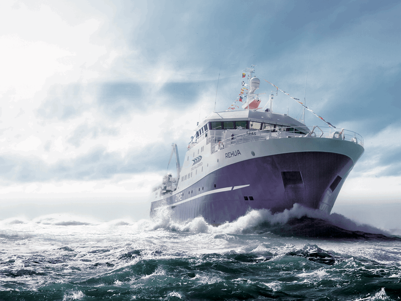 Large fishing vessel named Rehua sailing through rough ocean waves under a dramatic, cloudy sky.