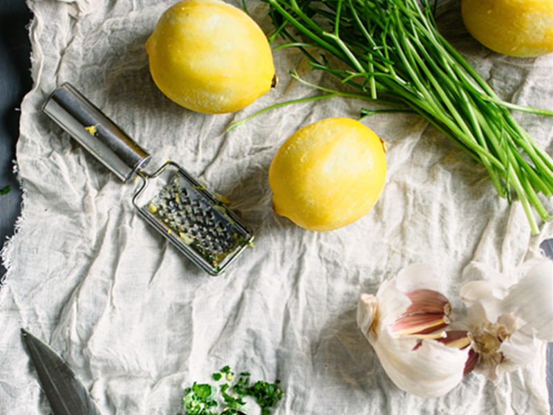 Fresh lemons, garlic, and herbs on a rustic linen cloth with a metal grater and a knife