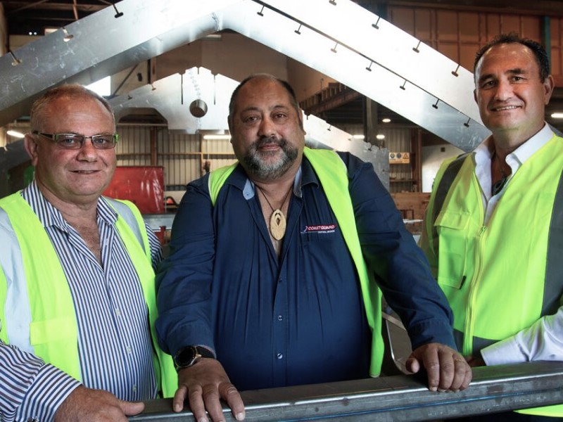 Three Sealord employees wearing high-visibility gear standing together inside a seafood processing factory.