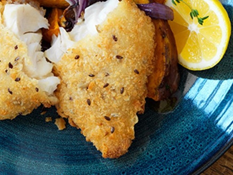 close up photo of crumbed fish on blue plate with lemon and salad beside it