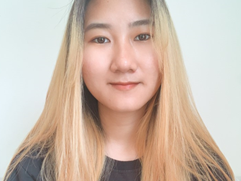 Young woman with blonde hair wearing a black top, taking a selfie against a plain white background