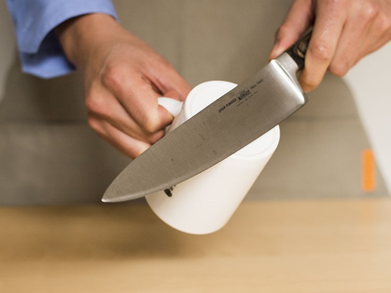 Person sharpening a kitchen knife using the unglazed bottom of a ceramic mug.