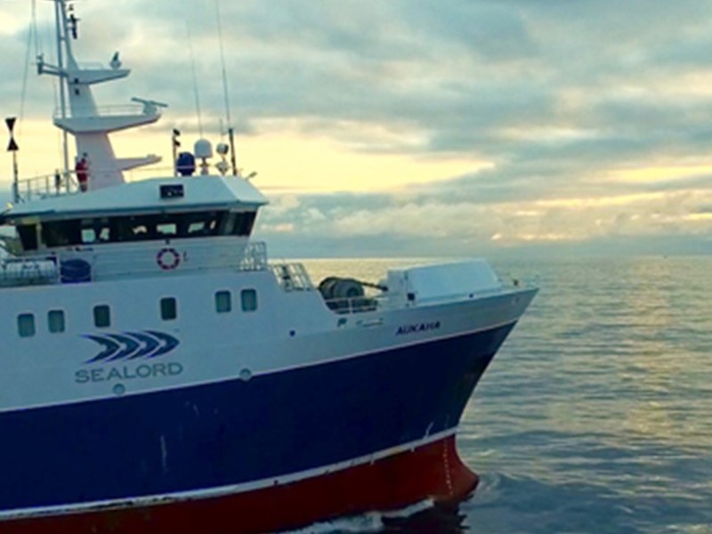 Front end of Sealord’s blue and white fishing vessel with company logo visible, out at sea against the open ocean backdrop.