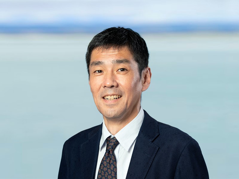 man standing infront of the sea in a black and white suit, he has short dark hair