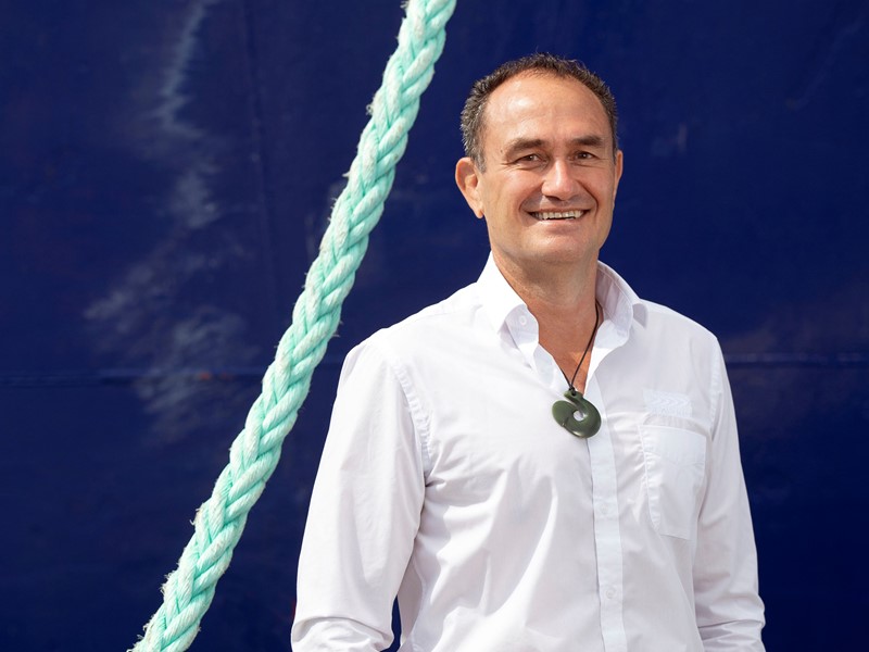 man standing in front of sealords boat in a white shirt, with a braided green rope hanging beside him on the left side.