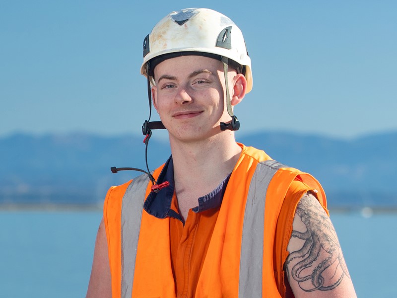 sealord worker with a safety hat high visibility clothes standing in front of the sea and mountains in the far background