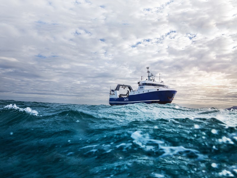 Sealord fishing vessel navigating open ocean waters under a cloudy sky, with gentle waves in the foreground and the sun peeking through the horizon.