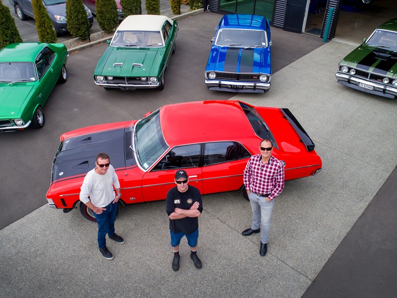 Bird’s-eye view of three men standing in front of five classic cars—red, blue, and red—at the Sealord Charity Classic Car Show. held in Nelson nz