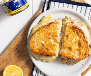 Cracked pepper tuna toastie from Sealord’s recipe range, cut in half and served on a white plate atop a wooden chopping board, with half a lemon in the bottom left and a can of Sealord tuna in the top left.